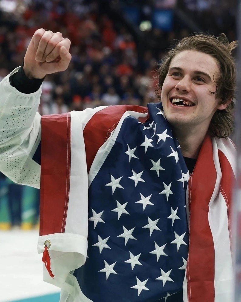 May include: A person smiling and celebrating, draped in an American flag. The flag has red and white stripes and a blue field with white stars. The person is wearing a white jacket.