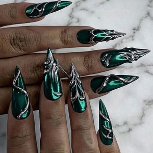 Può includere: Unghie artificiali lunghe e appuntite a stiletto con una finitura metallizzata verde smeraldo intenso. Ogni unghia è decorata con accenti cromati argentati in rilievo, simili a metallo liquido, che creano motivi organici e fluidi.