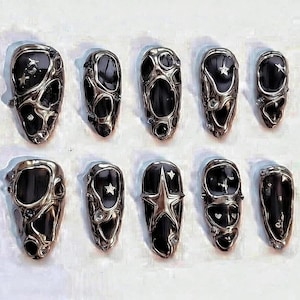 May include: A set of ten press-on nails featuring a black base with a raised, liquid-like silver metallic overlay. The design includes various cutouts, small embedded star shapes, and tiny clear rhinestones integrated into the textured silver surface.