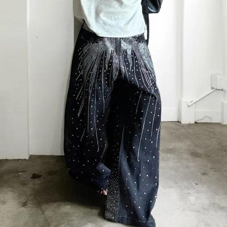 Unisex Rhinestone Pants | Wide Leg Studded Jeans | Glitter Streetwear Fashion Bottoms
.
Wide-leg black pants decorated with cascading rhinestones and glitter stud details shown in a studio setting.