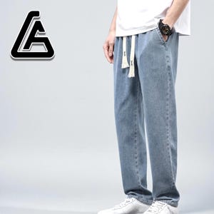 May include: Light blue denim pants with a drawstring waist. The pants have a relaxed fit and are paired with white sneakers. A white t-shirt is worn on top. The pants are a casual style.