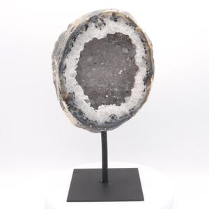 May include: A halved geode, showcasing a crystalline interior. The outer shell is a blend of grey, brown, and white, displayed on a black metal stand with a square base. A natural decorative item.