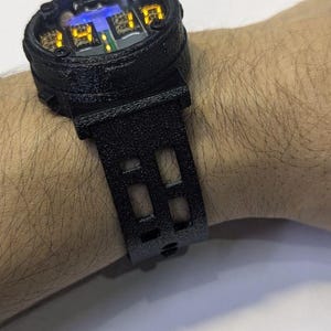 Könnte beinhalten: Schwarze Digitaluhr mit strukturiertem Armband und Gehäuse. Das Zifferblatt zeigt beleuchtete Zahlen und eine kartenartige Grafik. Die Uhr wird am Handgelenk getragen.