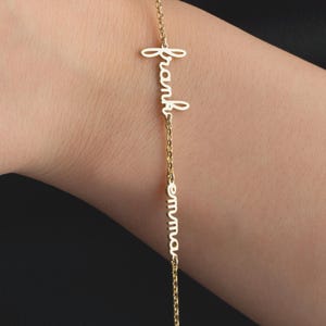 Könnte beinhalten: Ein zartes, goldfarbenes Armband mit den Namen "frank" und "emma" in Schreibschrift. Das Armband wird am Handgelenk getragen, wobei die Kette und die Namen gut sichtbar sind. Es handelt sich um ein personalisiertes Schmuckstück.