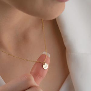 May include: A delicate gold necklace with a small, round pendant. The pendant has the name "Rachel" inscribed in cursive script. The necklace is shown against a white background.