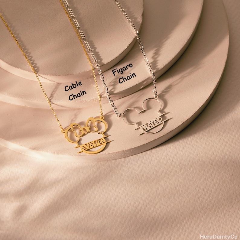 Peut inclure: Deux colliers personnalis&eacute;s avec un motif de t&ecirc;te de Mickey Mouse. L'un est dor&eacute; avec une cha&icirc;ne c&acirc;ble et le nom "EVELON". L'autre est argent&eacute; avec une cha&icirc;ne Figaro et le nom "MATEO".