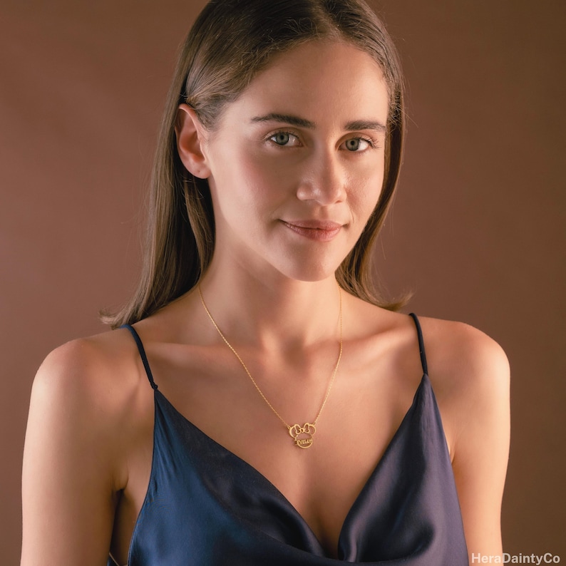 Peut inclure: Un collier dor&eacute; avec un pendentif en forme de couronne. Le pendentif comporte un petit c&oelig;ur et le mot "Queen" &eacute;crit en cursive. Le collier est port&eacute; par une personne v&ecirc;tue d'un haut en satin bleu fonc&eacute;.