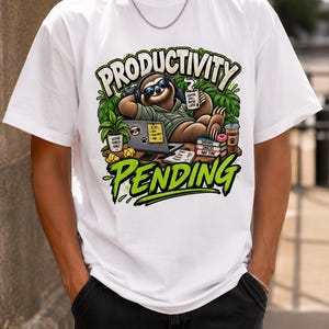 Könnte beinhalten: Ein weißes T-Shirt mit einer Grafik eines Faultiers mit Sonnenbrille und Kopfhörern, das an einem Schreibtisch mit Laptop, Kaffeetasse und Büchern liegt. Der Text "PRODUCTIVITY" und "PENDING" ist in fetten grünen Buchstaben abgebildet.
