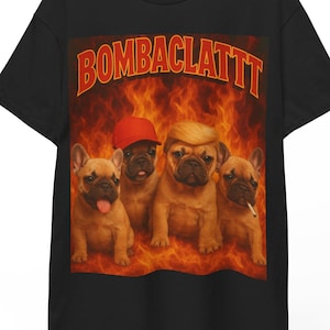 Pode incluir: Camiseta preta com um gráfico de quatro Bulldogs franceses em frente a um fundo flamejante. A palavra "BOMBA CLATTT" é impressa em laranja acima dos cães. Um cão usa um boné vermelho, outro tem um cigarro.
