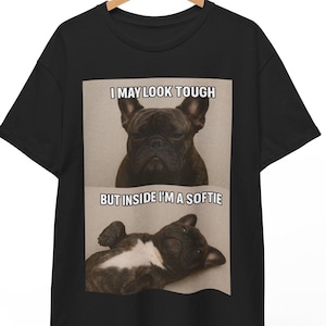 Pode incluir: Camiseta preta com um gráfico de um buldogue francês. O texto "I MAY LOOK TOUGH BUT INSIDE I'M A SOFTIE" está acima e abaixo da imagem do cão. O cão é mostrado em duas poses, uma séria e outra relaxada.