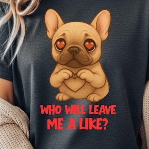 Pode incluir: Camiseta cinza escuro com um buldogue francês de desenho animado com olhos em forma de coração e um gesto de coração com as patas. O texto vermelho diz: "QUEM VAI ME DAR UM LIKE?" A camiseta é feita de tecido macio.