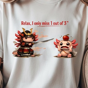 May include: White t-shirt with the text "Relax, I only miss 1 out of 3". The shirt features a cartoon samurai axolotl with a sword and another axolotl with an apple on its head. The axolotls are in a cartoon style.
