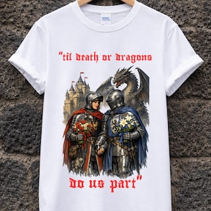 Può includere: T-shirt bianca con un design a tema medievale. Il disegno presenta due cavalieri in armatura, un drago e un castello. Il testo "'til death or dragons do us part" è stampato in rosso.