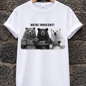 May include: White t-shirt with the text "WE'RE INNOCENT!" above a graphic of three bears in a police lineup. The bears are a brown bear, a black bear, and a polar bear, each with a police dept. ID. A humorous design.