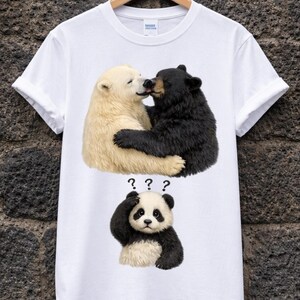 Può includere: T-shirt bianca con una grafica di due orsi che si baciano, uno nero e uno color crema. Sotto, un panda con un'espressione confusa e punti interrogativi. Un design umoristico.