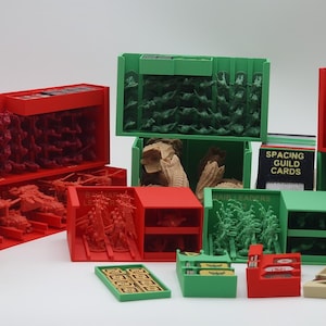 Puede incluir: Una colección de organizadores de juegos rojos, verdes y beige llenos de figuras en miniatura y componentes de juego. Los organizadores son de varios tamaños y formas, incluyendo cajas y bandejas. Una caja de cartas dice "Spacing Guild Cards".