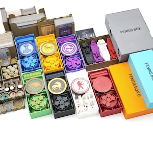 Może przedstawiać: Zestaw pudełek i komponentów do przechowywania gier planszowych. Obraz przedstawia różne kolorowe tace, żetony i elementy gier, w tym pudełka z napisem "FENRIS BOX" i "FENRIS BOX A". Komponenty są uporządkowane w kartonowych i plastikowych pojemnikach.