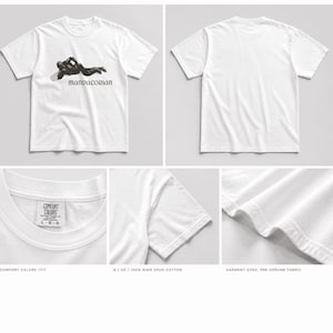 May include: White t-shirt featuring a black graphic of a figure and the word "MANDALORIAN". The shirt is made of 6.1 oz ring spun cotton. The image also shows details of the shirt's collar, sleeve, and hem.