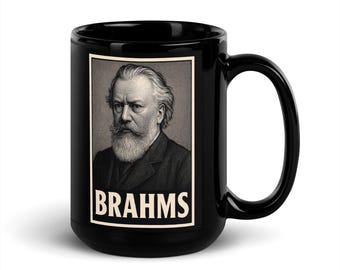 Op de afbeelding: Zwarte keramische mok met een portret van Johannes Brahms in een zwart-wit kader. Het woord "BRAHMS" is in witte, vette letters onder het portret gedrukt. De mok heeft een gebogen handvat.