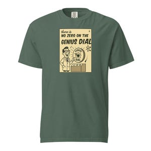 Può includere: T-shirt verde scuro con grafica vintage. La grafica presenta uno scienziato dei cartoni animati e il testo "there is NO ZERO ON THE GENIUS DIAL" su sfondo beige. L'illustrazione è in bianco e nero. La maglietta ha maniche corte e girocollo.