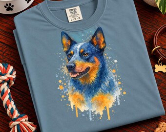 May include: A slate blue crew neck t-shirt featuring a watercolor-style illustration of a blue heeler dog. The dog has blue and tan fur, pointed ears, and an open mouth. The shirt has a Comfort Colors brand label at the neck with size L G G.
