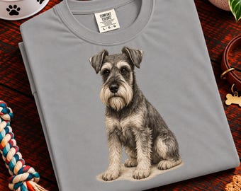 May include: A grey crew neck t-shirt featuring a detailed illustration of a seated Schnauzer dog with grey and tan fur. The shirt has a Comfort Colors brand label at the inner neckline with the size L-G-G clearly printed on the white fabric tag.