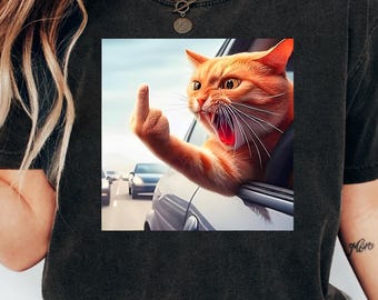 May include: Black t-shirt featuring a graphic of an orange cat extending its paw with the middle finger up, out of a car window. The cat has an angry expression with its mouth open. Cars are visible in the background.