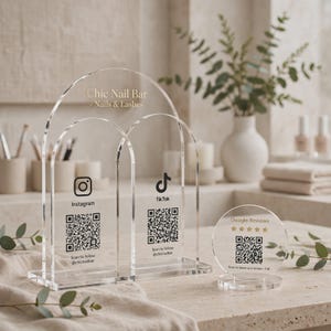 May include: A clear acrylic sign set featuring a double-arched display with Chic Nail Bar - Nails & Lashes text, Instagram and TikTok logos, and QR codes, alongside a circular sign with Google Reviews text, five stars, and a QR code.