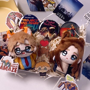 May include: A gift box containing two plush dolls, three circular pin-back buttons, and two acrylic keychains featuring Project Hail Mary themes. The items include stickers with text such as Project Hail Mary, Amaze, and My Bump, nestled in shredded paper.