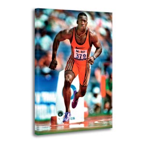 Puede incluir: Impresión en lienzo de un atleta corriendo. Viste un uniforme de carrera naranja y negro con el número 379. El logotipo de Nike es visible. El fondo está borroso, sugiriendo movimiento y velocidad.