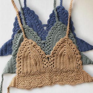 Puede incluir: Tres tops de ganchillo hechos a mano en tonos beige, verde grisáceo y azul. Cada top presenta un diseño de cuello en V con bordes festoneados y delicadas correas. Los tops están hechos de hilo suave.