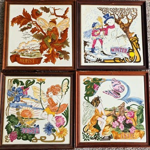 May include: A set of four framed ceramic tiles, each depicting a fairy scene representing different seasons. The illustrations include fairies with autumnal leaves, a snowman, flowers, and a butterfly. The tiles are framed in dark wood and feature the words "HERFST", "WINTER", "ZOMER", and "LENTE".