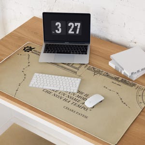 Op de afbeelding: Een bureau-opstelling met een laptop, toetsenbord en muis op een grote rechthoekige bureaumat. De mat heeft een vintage kaartontwerp met Italiaanse tekst. Een digitale klok toont 3:27.