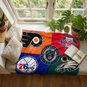 Op de afbeelding: Een zachte fleece deken met een collage van logo's van sportteams uit Philadelphia, waaronder de Flyers, Phillies, 76ers, Union en Eagles, weergegeven in levendige oranje, rode, blauwe en groene kwadranten met een centraal rond embleem.