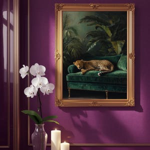 Puede incluir: Un cuadro enmarcado en oro representa un leopardo descansando sobre un sofá de terciopelo verde, con un fondo de exuberante vegetación. El marco dorado ornamentado añade un toque de elegancia. La obra de arte está colgada en una pared morada.
