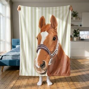May include: A rectangular fleece blanket featuring a large, detailed illustration of a brown horse head with a white blaze on its forehead and a dark brown halter, set against a background of vertical light green and white stripes.