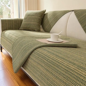 May include: A white ceramic mug with a black handle and the text "But First, Coffee" in a bold, black font. The mug is set against a blurred background, suggesting a cosy setting.