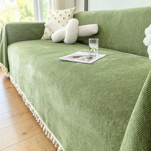 May include: A green sofa with a matching cover featuring a herringbone pattern. Decorative pillows in white and yellow dot patterns rest on the sofa. A glass of water and a magazine are on the sofa.