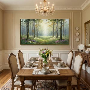 May include: A large rectangular landscape painting depicting a sunlit forest scene with tall trees, green foliage, and patches of purple and white wildflowers, framed in a thin gold border and mounted on a beige wall above a wooden dining table.