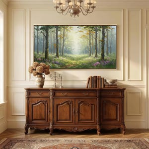 May include: A rectangular landscape painting of a sunlit forest with tall trees, green grass, and purple wildflowers, displayed in a thin frame above a dark brown wooden sideboard featuring four cabinet doors, drawers, and decorative metal hardware.