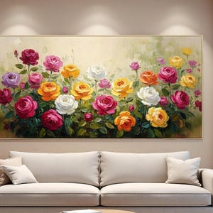 Op de afbeelding: Een ingelijst olieverfschilderij met een levendige reeks rozen in tinten rood, roze, geel, oranje en wit. Het kunstwerk toont een weelderige tuinscène met groene bladeren en een zachte, neutrale achtergrond. Het schilderij wordt boven een beige bank weergegeven.
