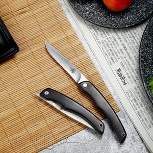 May include: Two folding knives with silver-toned metal blades and dark wooden handles. One knife is fully extended, showing a sharp pointed tip and a circular logo on the blade. The second knife is folded shut, displaying a curved handle and a metal pivot pin.