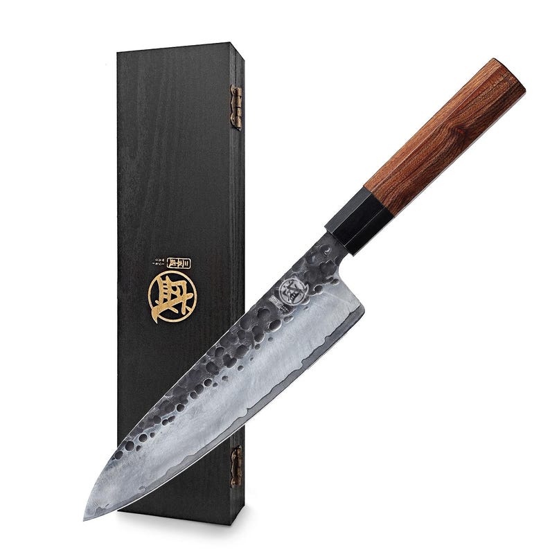 May include: A Japanese-style chef's knife with a wooden handle and a textured, silver-colored blade. The knife is displayed next to a black wooden box with gold accents. The blade has a unique hammered finish.