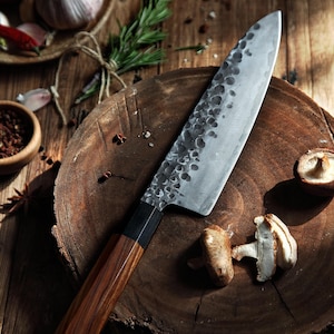 May include: A handcrafted chef's knife with a wooden handle and a textured, silver-colored blade. The knife rests on a wooden cutting board, alongside mushrooms and spices, suggesting a culinary theme.