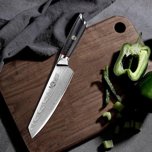 May include: A stainless steel chef's knife with a patterned blade and a black wooden handle. The knife is on a wooden chopping board next to a green pepper. The knife has a silver bolster and a red accent.