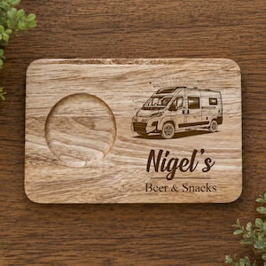 May include: A rectangular wooden serving board featuring a circular cutout on the left side. The board is engraved with a camper van illustration and the text "Nigel's Beer & Snacks" in a dark brown script and sans-serif font style.