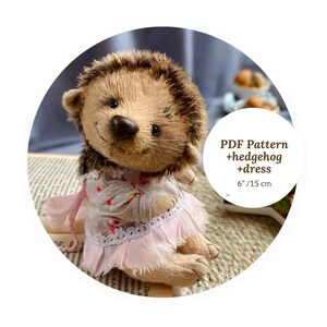 May include: A handmade plush hedgehog doll wearing a pink dress with floral accents and a lace trim. The doll has a detailed face and a spiky back. The image includes the text "PDF Pattern +hedgehog +dress 6"/15 cm".