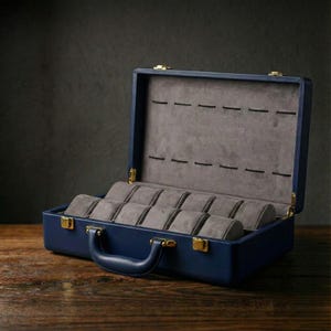 May include: A navy blue watch case with a handle and gold-colored hardware. The interior is lined with gray fabric and features individual compartments for storing multiple watches. The case is open, revealing the watch storage.