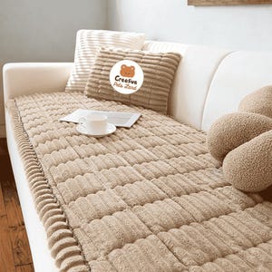 May include: A beige pet bed cover with a ribbed texture, placed on a white sofa. A matching pillow with the text "Creative Pets Land" is visible. A white teacup and saucer sit on a small tray.