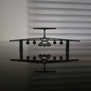 May include: A black metal airplane model with detailed wings, engines, and tail. The model is displayed on a reflective surface, creating a mirrored image. The design is intricate, showcasing the aircraft's structure.